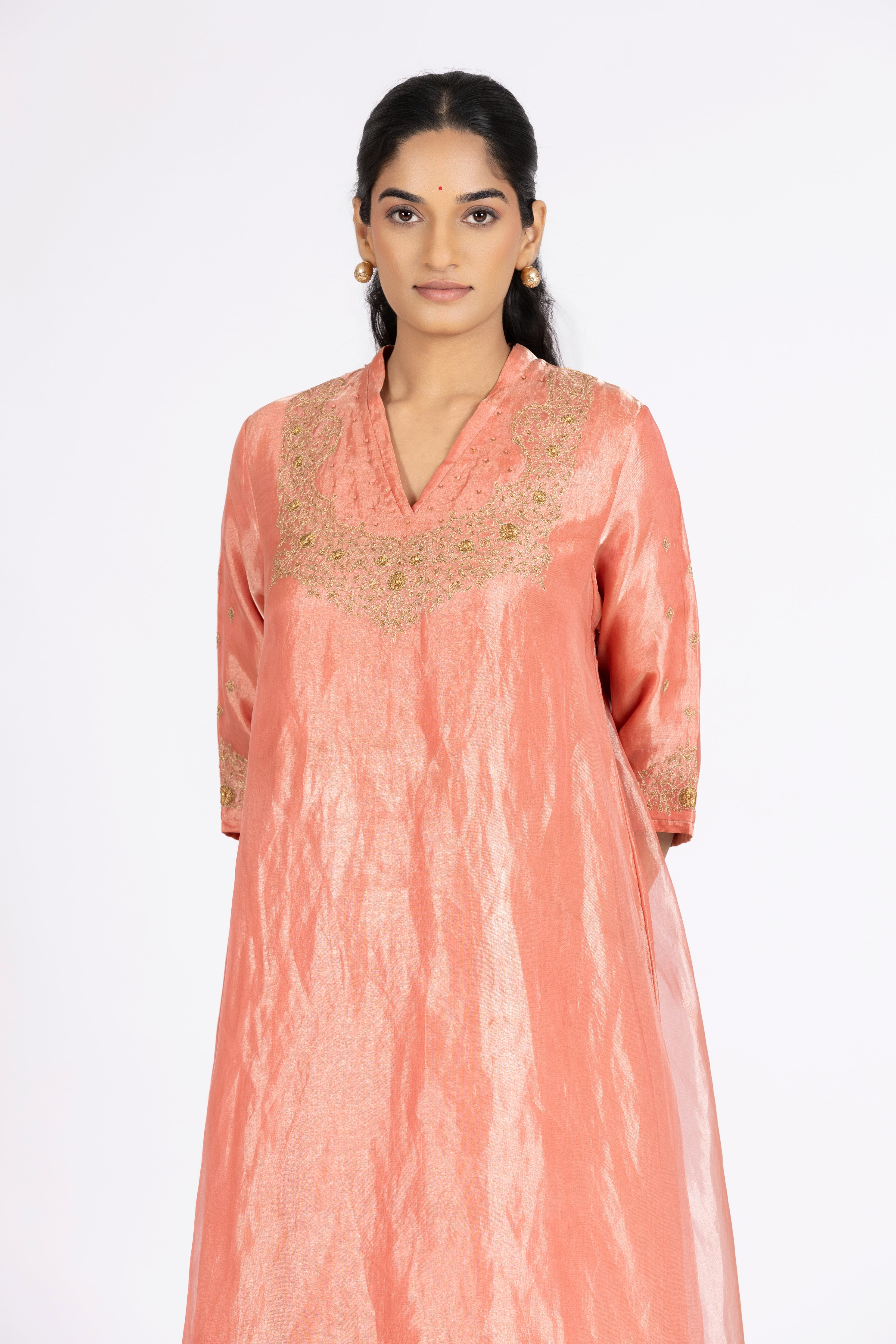 Woman wearing a peach-colored kurta with intricate embroidery on a white background