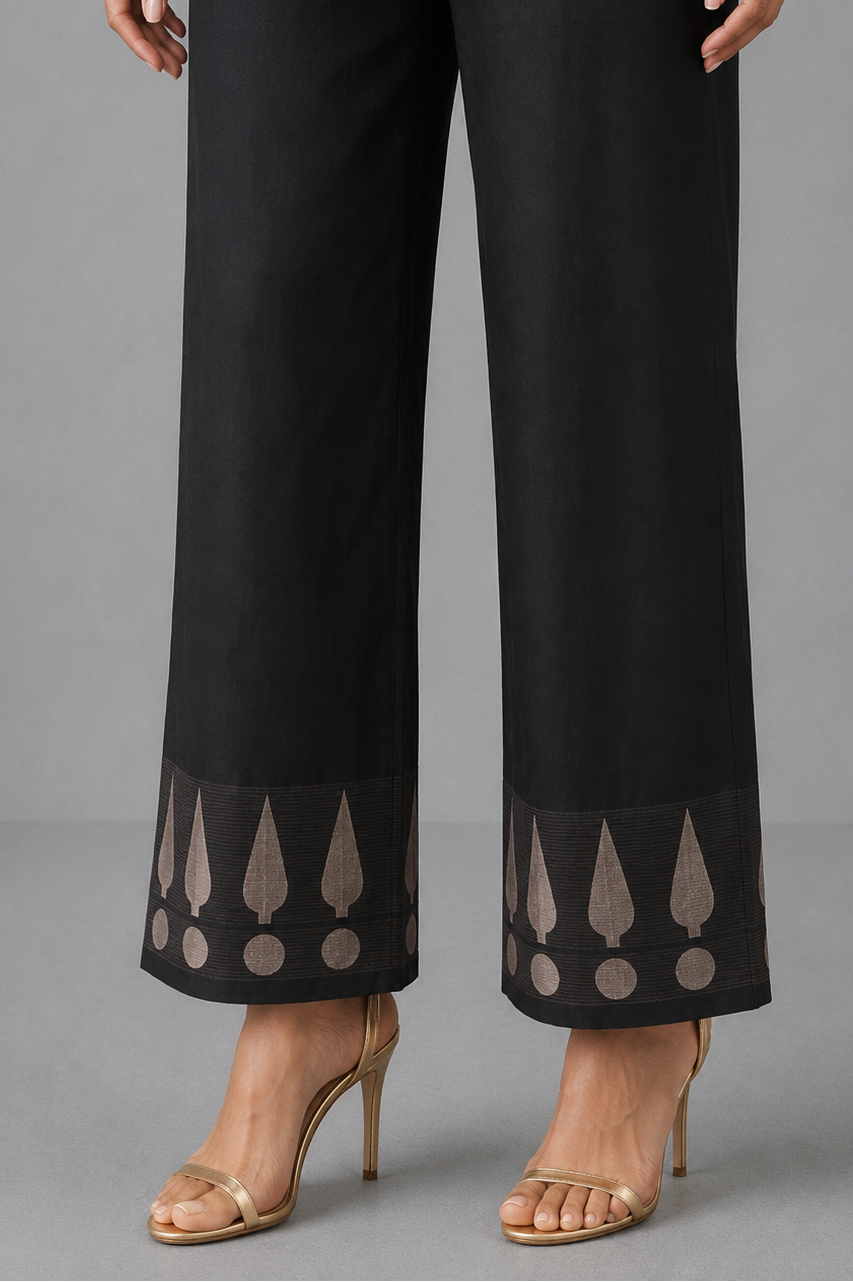 Black wide-leg cropped pants with sheer lace trim at the hem featuring beige teardrop and circle motifs, shown on a model wearing gold high-heeled sandals against a gray studio background.